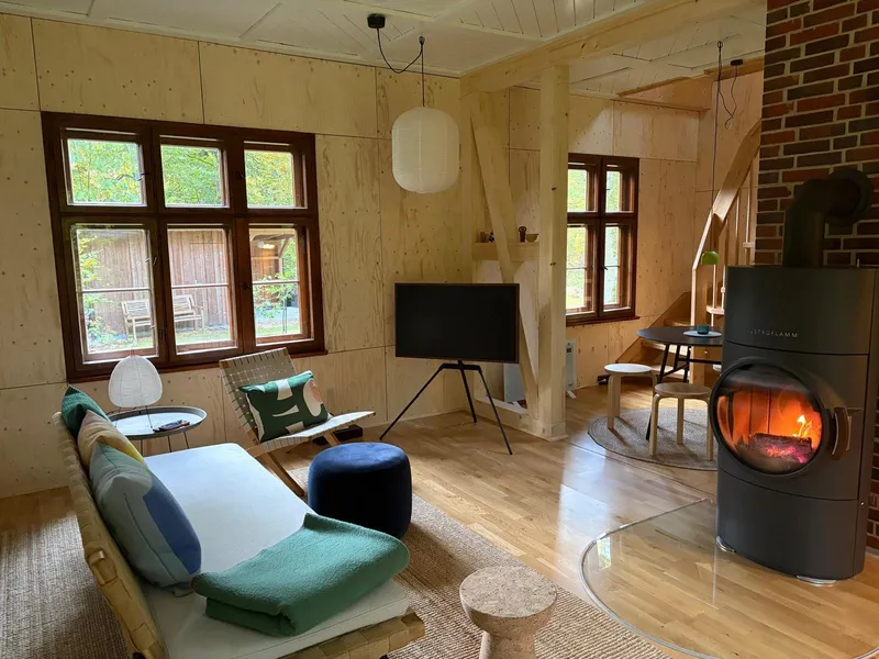 Wohnraum mit Kaminofen, Sofa und Essplatz in hellem Holz